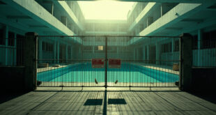 Empty public swimming pool behind locked gate with prohibition signs at a border area facility