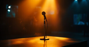 Lone microphone stands silent on broadcast desk in empty television studio bathed in golden and blue stage lights