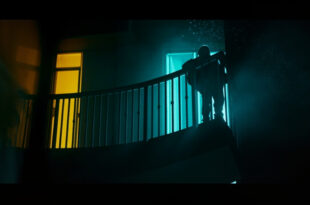 Empty hotel balcony at night with damaged safety barrier, illuminated by contrasting dark blue and yellow lighting