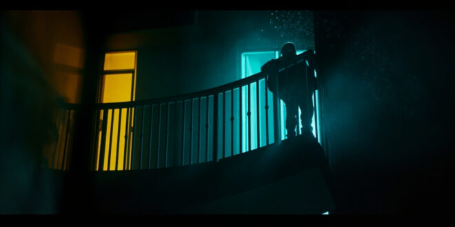Empty hotel balcony at night with damaged safety barrier, illuminated by contrasting dark blue and yellow lighting
