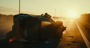 Overturned luxury car wreckage abandoned on empty Spanish highway at dawn, with atmospheric lighting in gray and gold
