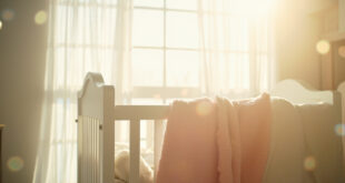 Empty white crib with soft blankets in a sunlit nursery room, awaiting a new arrival