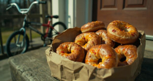 Golden brown jalapeño cheddar bagels arranged in paper delivery bag next to BMX bicycle on residential driveway
