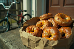 Golden brown jalapeño cheddar bagels arranged in paper delivery bag next to BMX bicycle on residential driveway