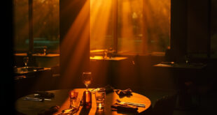 Empty round table with multiple place settings and one highlighted chair in a dimly lit restaurant, evoking solitude.