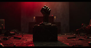 Bronze fist sculpture on marble base in dimly lit room with dramatic shadows