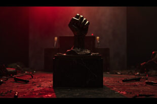 Bronze fist sculpture on marble base in dimly lit room with dramatic shadows