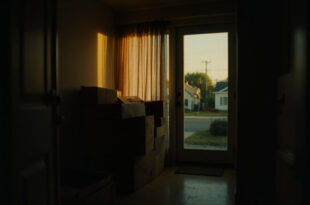 Moving boxes and personal belongings near doorway of quiet family home with soft natural lighting.