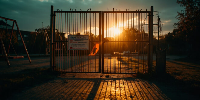 Locked playground gate with warning signs blocking access to empty playground equipment at dusk, symbolizing exclusion