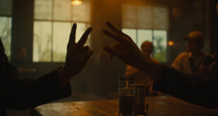 Hands forming sign language gesture above restaurant table with warm lighting and wooden dining tables in soft focus.