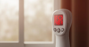 Digital thermometer displaying high temperature reading in poorly ventilated modern apartment interior.