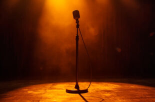 Vintage microphone standing alone on dimly lit Grand Ole Opry wooden stage with burgundy curtains and amber spotlight
