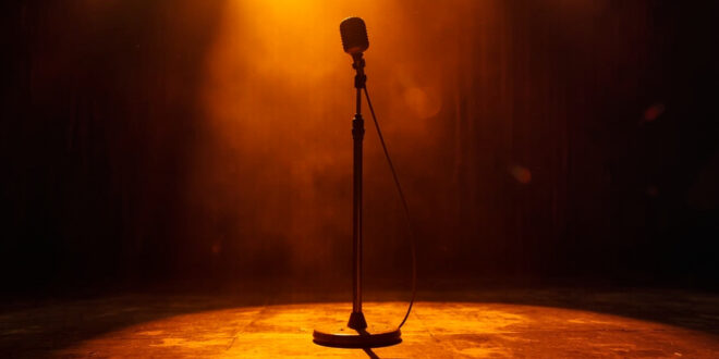 Vintage microphone standing alone on dimly lit Grand Ole Opry wooden stage with burgundy curtains and amber spotlight