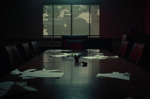 Empty conference room with microphone on wooden table, papers scattered, venetian blind shadows across chairs.
