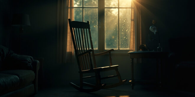 Empty rocking chair beside window in dimly lit living room at dusk, with wilted flower on wooden table