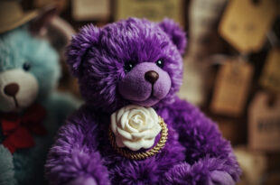 Purple commemorative bear toy with white rose emblem displayed against neutral background with soft lighting