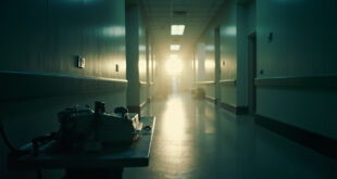 Abandoned medical equipment including defibrillator on metal table in empty prison infirmary corridor at dawn