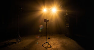 Abandoned television studio with unmanned equipment, a lone microphone on empty stage illuminated by dim gold lighting