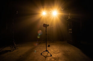 Abandoned television studio with unmanned equipment, a lone microphone on empty stage illuminated by dim gold lighting