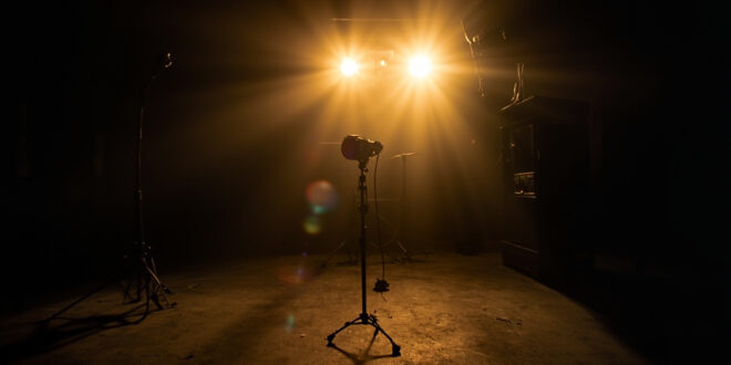 Abandoned television studio with unmanned equipment, a lone microphone on empty stage illuminated by dim gold lighting