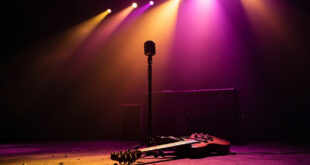 Vintage microphone stand on empty stage with lone electric guitar resting against amplifier in abandoned concert venue