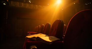 Abandoned Broadway theater with empty seats facing a vacant stage, vintage script resting on a seat in dim burgundy and amber light.