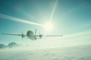 Solitary aircraft flying over snowy Alaskan wilderness approaching distant airport under vast arctic blue sky