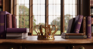 Golden crown sits on wooden desk next to open books and school supplies in elegant library setting.