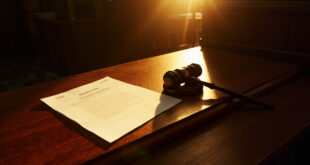 Ornate wooden gavel beside billion-dollar lawsuit documents on a mahogany desk in an empty courtroom with dramatic lighting.