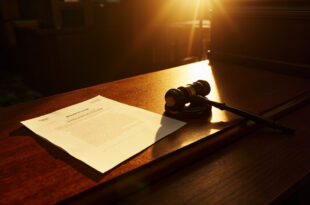 Ornate wooden gavel beside billion-dollar lawsuit documents on a mahogany desk in an empty courtroom with dramatic lighting.