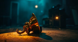 Solitary Grammy trophy sits on empty wooden table in abandoned recording studio at twilight, bathed in gold and blue light