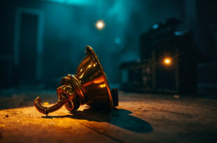 Solitary Grammy trophy sits on empty wooden table in abandoned recording studio at twilight, bathed in gold and blue light