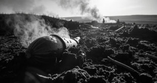 Rusty wartime shell casing protruding from blackened peat moss with smoke drifting across burned moorland hills