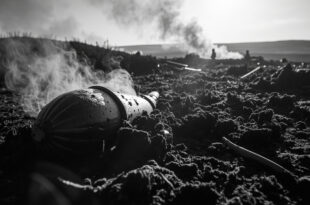 Rusty wartime shell casing protruding from blackened peat moss with smoke drifting across burned moorland hills