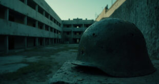 Weathered military helmet sits on concrete ledge in empty training facility courtyard with barracks buildings in background.