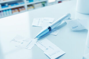 Medical injection pen device on pharmacy counter with price tags and pharmaceutical documentation.