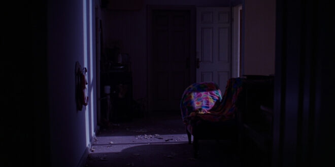 Dark hallway with closed door, colorful fabric draped nearby, scattered personal belongings on floor.