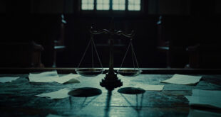 Bronze scales of justice on wooden courtroom desk with legal documents scattered around in dim lighting