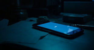Smartphone displaying chat interface on dark desk surrounded by legal papers and closed laptop with gavel reflection on screen