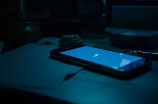 Smartphone displaying chat interface on dark desk surrounded by legal papers and closed laptop with gavel reflection on screen