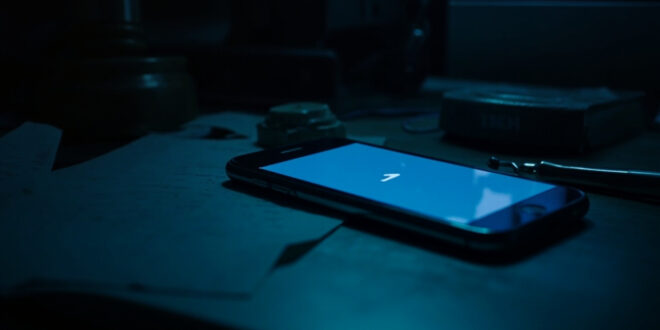 Smartphone displaying chat interface on dark desk surrounded by legal papers and closed laptop with gavel reflection on screen