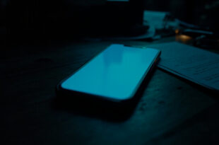 Smartphone with empty chat interface glowing on dark wooden surface surrounded by paper documents