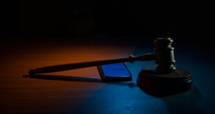 Wooden gavel beside glowing smartphone screen in dark courtroom setting with dramatic lighting