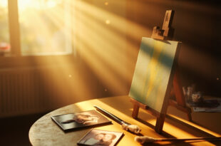 Empty art easel with finished family portrait in sunlit room, paintbrush resting beside canvas with art supplies and photos