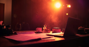 Empty writer's desk with typewriter, closed laptop and scattered script pages in a quiet television studio after hours