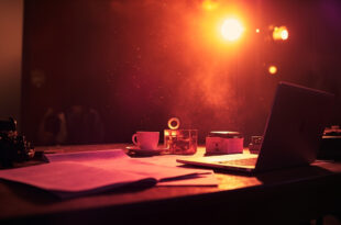 Empty writer's desk with typewriter, closed laptop and scattered script pages in a quiet television studio after hours