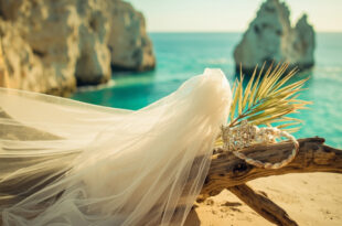 White bridal veil and accessories arranged on weathered driftwood against turquoise ocean backdrop in Cabo.