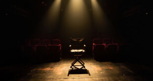 Empty Broadway theater stage with single director's chair under spotlight, red velvet seats in shadows