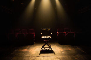 Empty Broadway theater stage with single director's chair under spotlight, red velvet seats in shadows