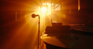 Empty recording studio at golden hour with reclaimed vinyl masters on mixing desk and abandoned microphone stand with sheet music
